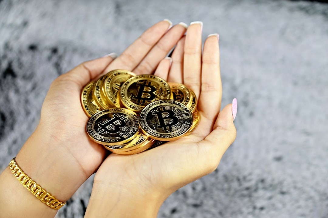 Hands holding a pile of shiny physical Bitcoins with a blurred background.